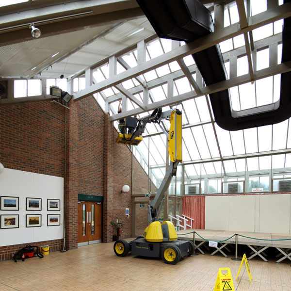 Cherry picker being used to clean inside glass of museum entrance.
